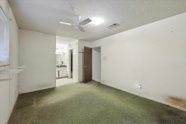 empty room featuring a textured ceiling, ceiling fan, visible vents, baseboards, and light carpet