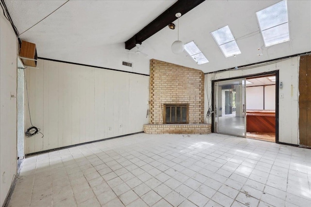 unfurnished living room with visible vents, vaulted ceiling with skylight, a fireplace, and wood walls