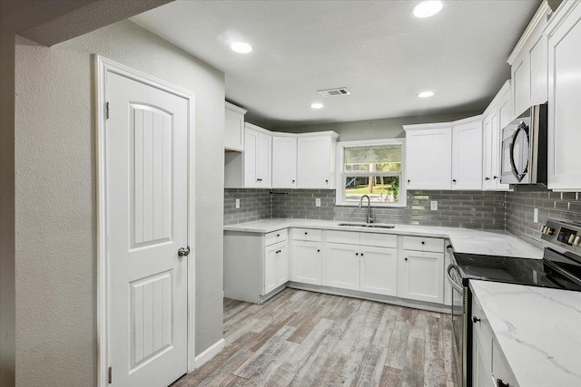 kitchen featuring sink, light stone countertops, appliances with stainless steel finishes, tasteful backsplash, and white cabinetry