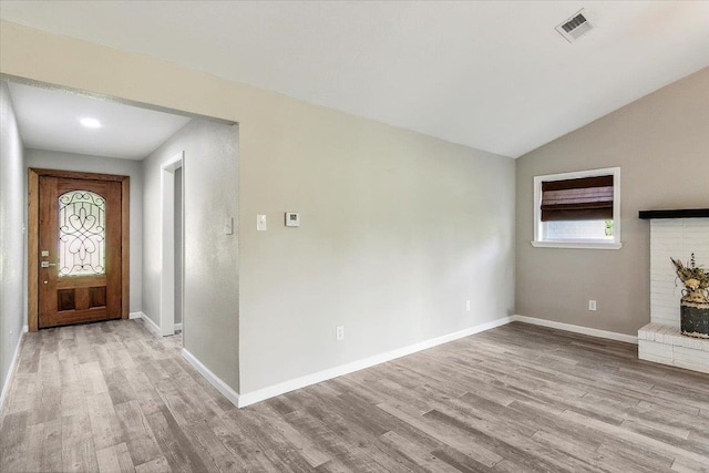 foyer entrance with a fireplace, light hardwood / wood-style flooring, and vaulted ceiling