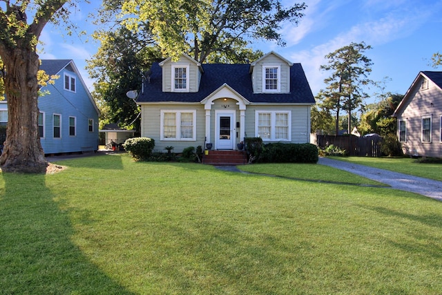 cape cod house featuring roof with shingles, fence, and a front yard