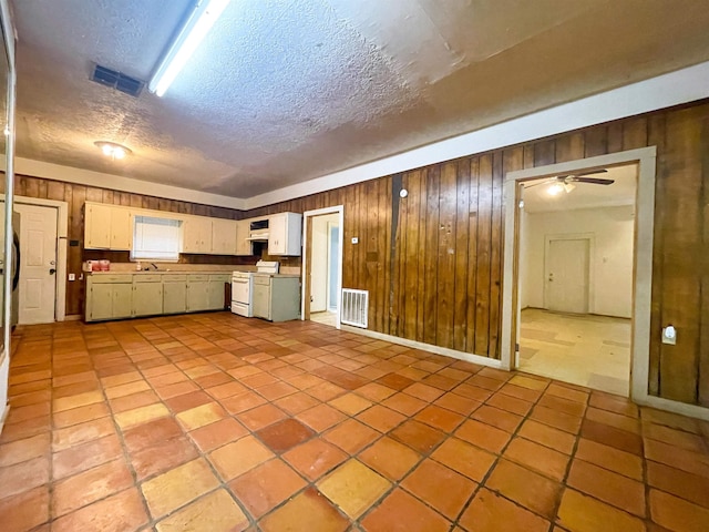 kitchen featuring stove, white cabinets, wooden walls, ceiling fan, and a textured ceiling