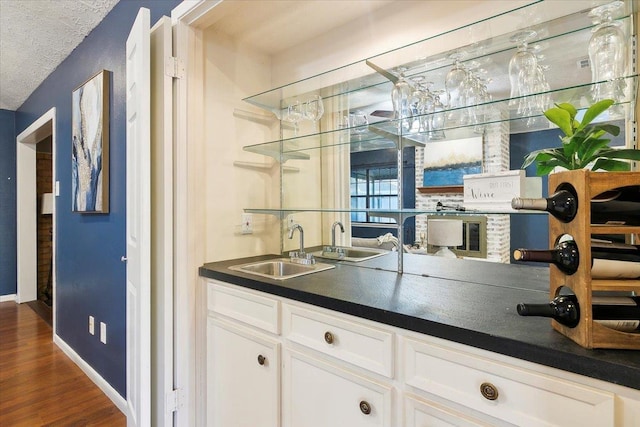 bar with white cabinets, a textured ceiling, dark wood-type flooring, and sink