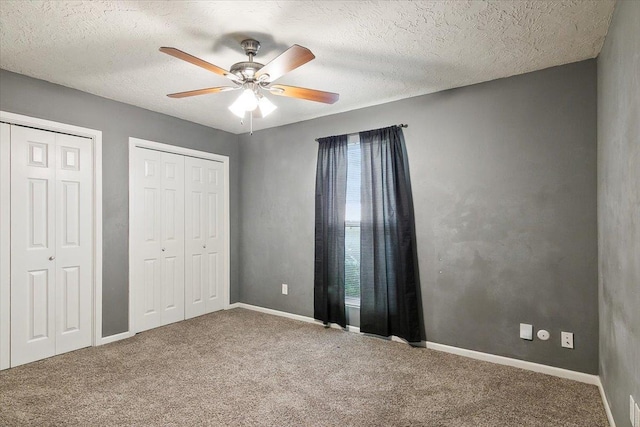 unfurnished bedroom with two closets, ceiling fan, a textured ceiling, multiple windows, and carpet floors