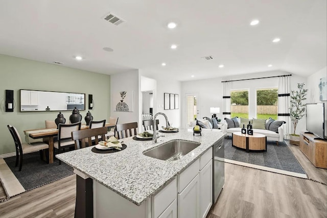 kitchen with visible vents, light wood finished floors, a sink, stainless steel dishwasher, and open floor plan