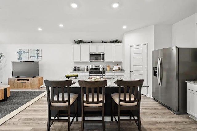 kitchen featuring light wood-type flooring, a sink, light stone counters, white cabinetry, and stainless steel appliances