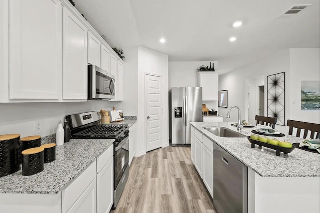 kitchen featuring a sink, light wood-style flooring, appliances with stainless steel finishes, white cabinets, and a kitchen island with sink