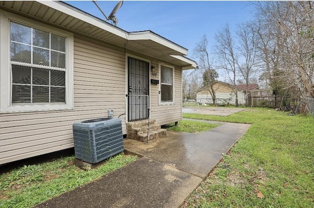 property entrance featuring a lawn, fence, and central air condition unit