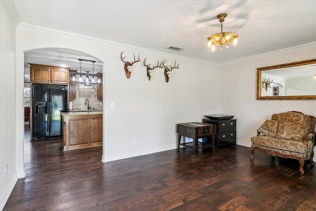 living area featuring an inviting chandelier, ornamental molding, sink, and dark wood-type flooring