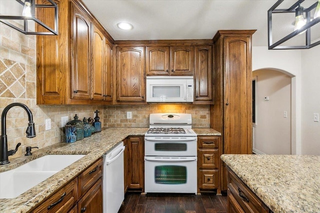 kitchen with light stone countertops, sink, dark hardwood / wood-style flooring, backsplash, and white appliances