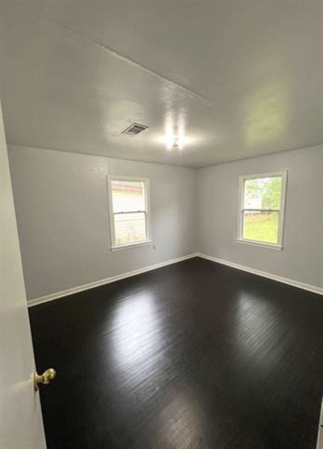 spare room featuring dark wood-style floors, visible vents, and baseboards