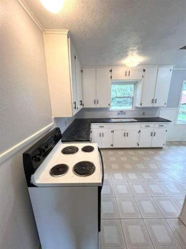 kitchen featuring a textured ceiling, light floors, white range with electric cooktop, and white cabinetry