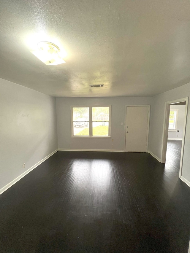 empty room with dark wood-style floors, baseboards, visible vents, and a textured ceiling