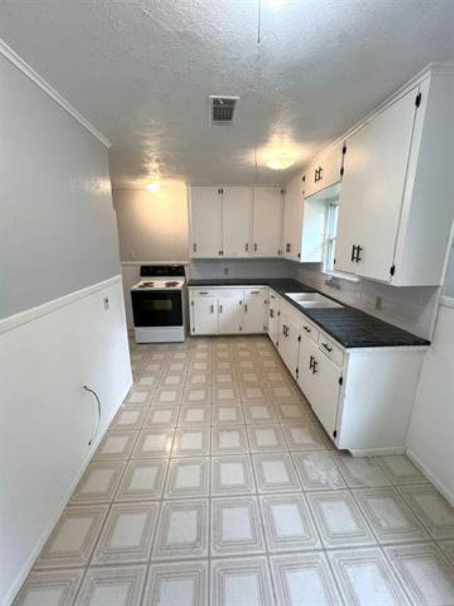 kitchen with white electric range oven, visible vents, dark countertops, white cabinetry, and a sink