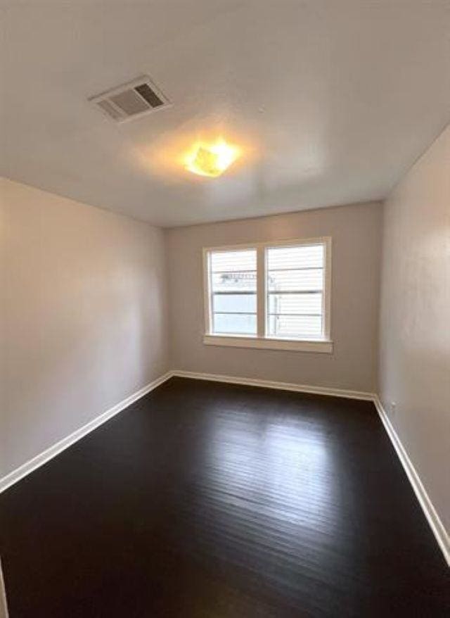 empty room with dark wood-style floors, visible vents, and baseboards