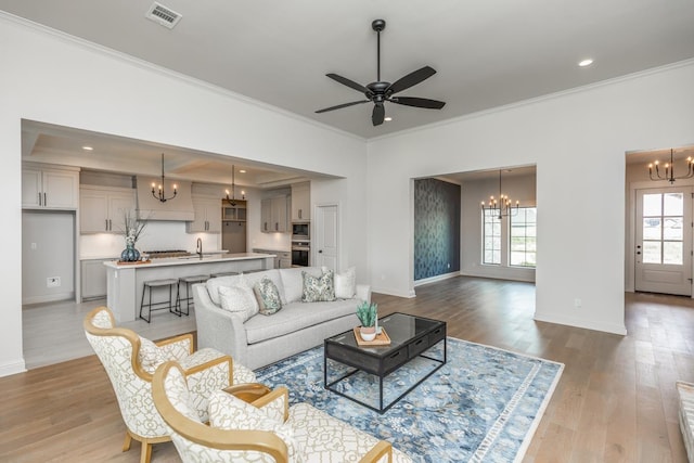 living room with ornamental molding, ceiling fan with notable chandelier, and light wood-type flooring