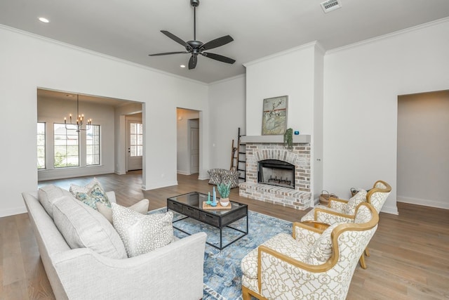 living room featuring a brick fireplace, ceiling fan with notable chandelier, light hardwood / wood-style flooring, and ornamental molding