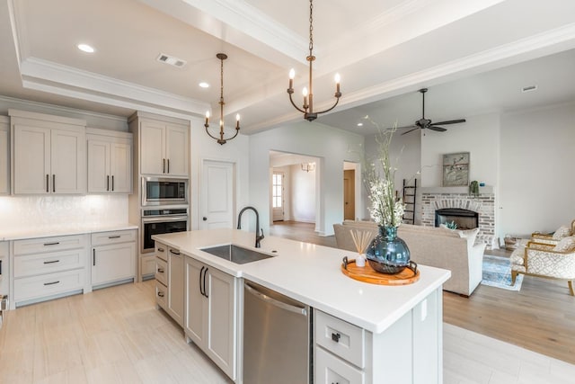 kitchen with pendant lighting, sink, stainless steel appliances, a tray ceiling, and a center island with sink