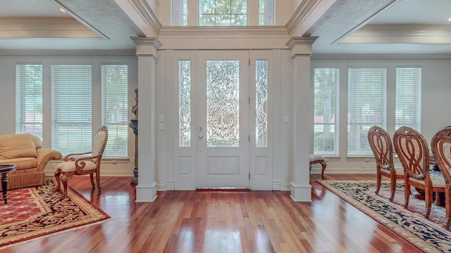 foyer with crown molding, wood finished floors, decorative columns, and a healthy amount of sunlight