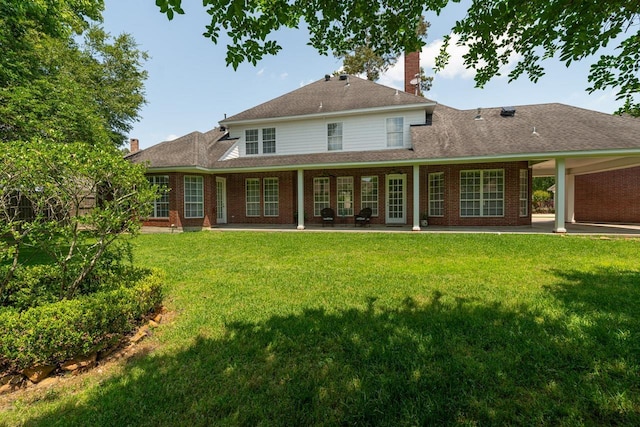 rear view of house featuring brick siding, a chimney, a lawn, and a patio area