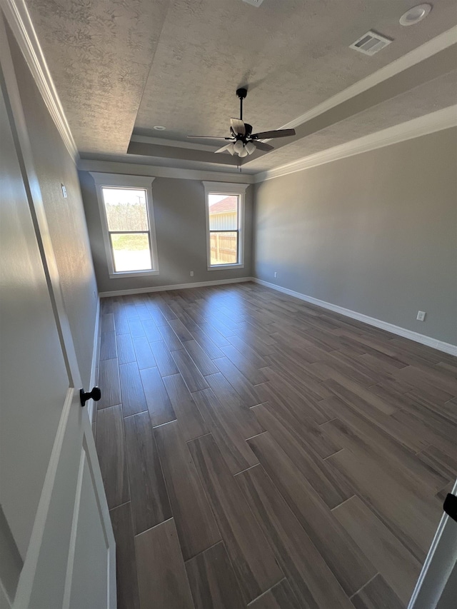 spare room with a textured ceiling, visible vents, baseboards, dark wood-style floors, and a raised ceiling