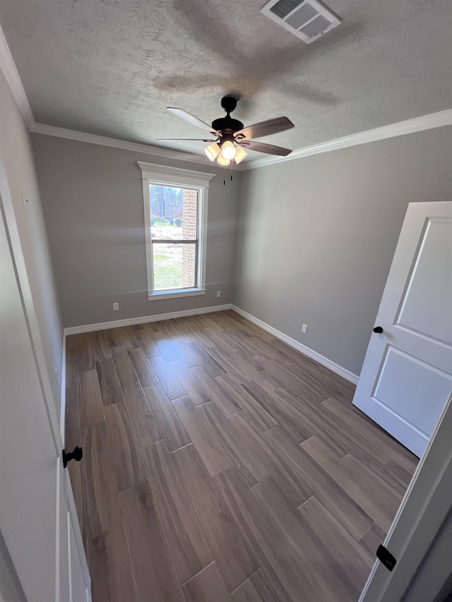 empty room with a textured ceiling, wood finished floors, visible vents, baseboards, and crown molding