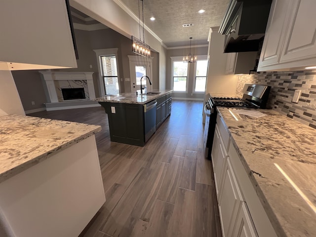 kitchen with a center island with sink, white cabinets, appliances with stainless steel finishes, ornamental molding, and hanging light fixtures