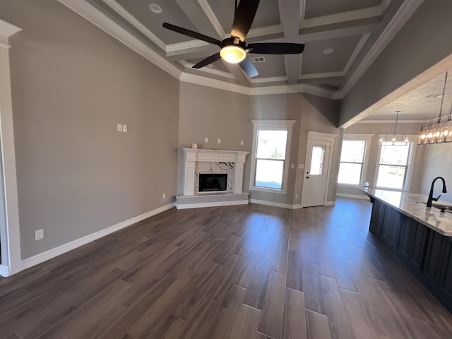 unfurnished living room featuring baseboards, coffered ceiling, dark wood-type flooring, a fireplace, and ceiling fan with notable chandelier