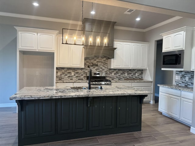 kitchen with light stone counters, built in microwave, pendant lighting, and a kitchen island with sink