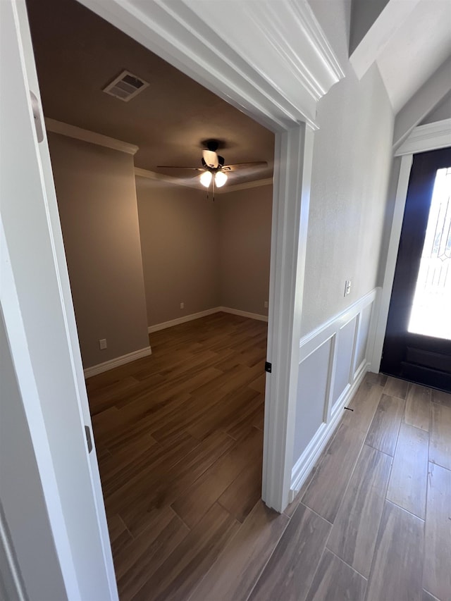 unfurnished room with a wainscoted wall, visible vents, wood finished floors, and ornamental molding