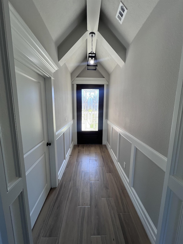 doorway to outside featuring visible vents, lofted ceiling, a wainscoted wall, dark wood-type flooring, and a decorative wall