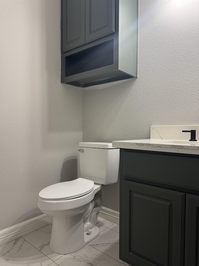 bathroom featuring marble finish floor, a textured wall, toilet, vanity, and baseboards