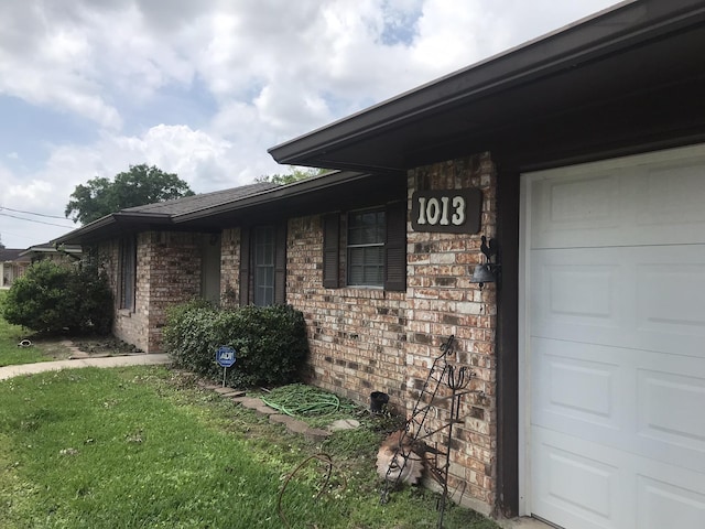 doorway to property with a garage, a lawn, and brick siding