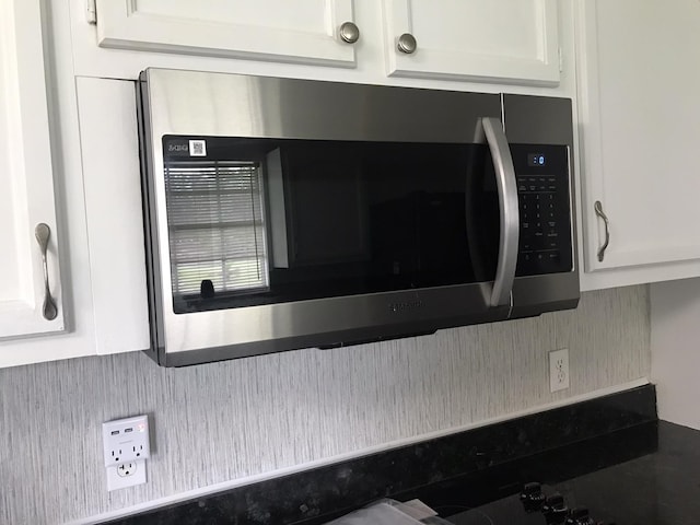 details featuring decorative backsplash, stainless steel microwave, white cabinets, and dark countertops