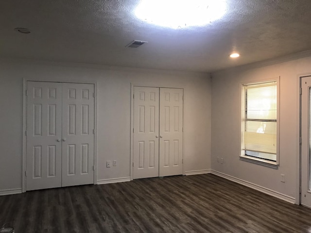 unfurnished bedroom featuring visible vents, baseboards, dark wood-style flooring, and two closets