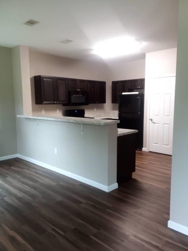 kitchen featuring black appliances, a kitchen breakfast bar, dark hardwood / wood-style flooring, and kitchen peninsula