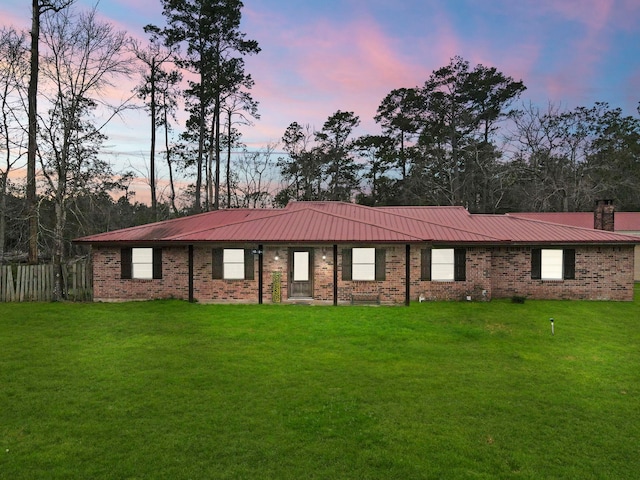 ranch-style house featuring brick siding, metal roof, a lawn, and a chimney