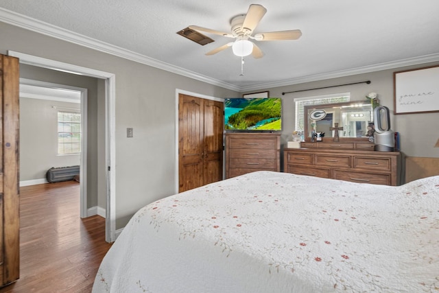 bedroom with crown molding, wood finished floors, baseboards, and a closet