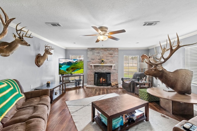 living area with a brick fireplace, wood finished floors, visible vents, and ornamental molding