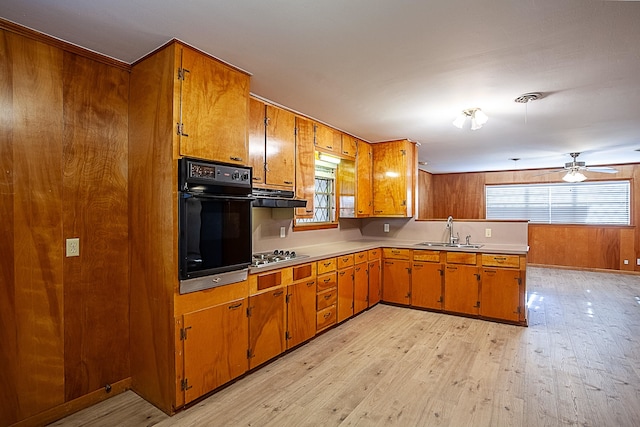 kitchen featuring light wood-type flooring, ceiling fan, sink, black oven, and stainless steel gas stovetop