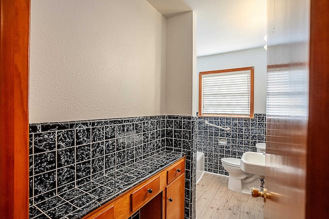 bathroom featuring wood-type flooring, toilet, and tile walls