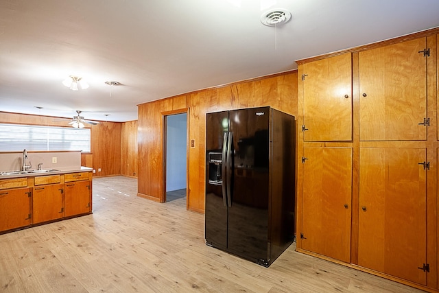 kitchen featuring black fridge, light wood-type flooring, sink, and wooden walls