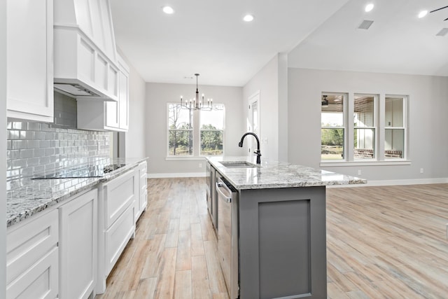 kitchen featuring decorative backsplash, light wood-style flooring, white cabinets, black electric cooktop, and a sink