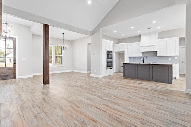 kitchen with a chandelier, open floor plan, decorative backsplash, light wood-style flooring, and white cabinetry