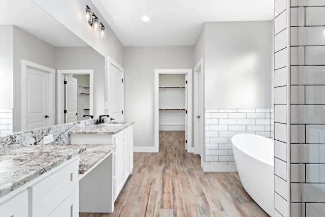 full bath with wood finished floors, vanity, tile walls, a soaking tub, and a spacious closet