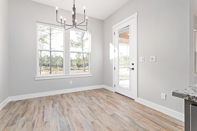 unfurnished dining area featuring an inviting chandelier, light wood-type flooring, and baseboards