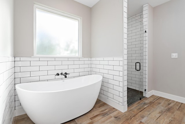 full bathroom featuring a shower stall, wainscoting, wood finished floors, a soaking tub, and tile walls