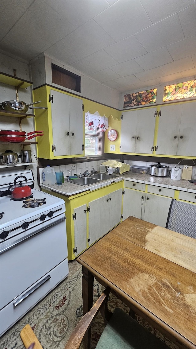 kitchen with backsplash, sink, white cabinets, and white stove