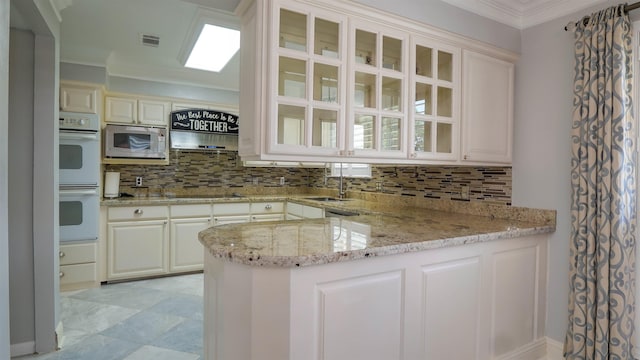 kitchen featuring a sink, stainless steel microwave, light stone counters, white double oven, and decorative backsplash