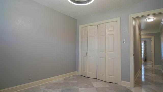 unfurnished bedroom with a closet, marble finish floor, baseboards, and ornamental molding